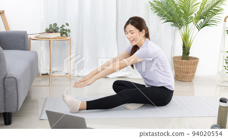 Beautiful Asian woman in sportswear is warming up or doing light exercises in the house with dumbbells and a protein shake or bottle of water and using a laptop at home, Healthy exercise. 94020554