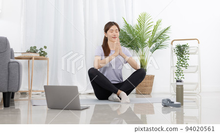 Beautiful Asian woman in sportswear is warming up or doing light exercises in the house with dumbbells and a protein shake or bottle of water and using a laptop at home, Healthy exercise. 94020561