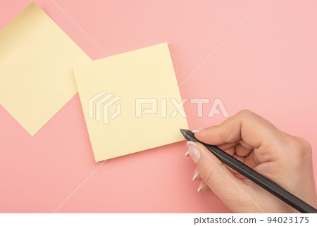 Hand written notes black pencil on yellow sticker. pink table background. woman hand writing on yellow sticky notes. Business people meeting and use notes to share idea on sticky note. 94023175