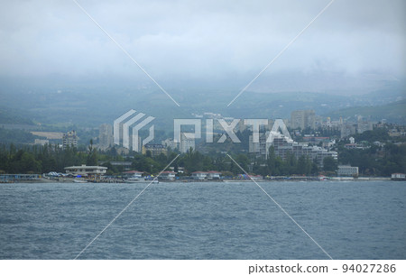 Resort town Gurzuf, buildings beach mountains plunged in a fog cloudy sky, view from the sea. Southern coast of the Black Sea, Crimea Resort town Gurzuf, buildings beach mountains plunged in a fog cloudy sky, view from the sea. Southern coast of the Black Sea, Crimea 94027286