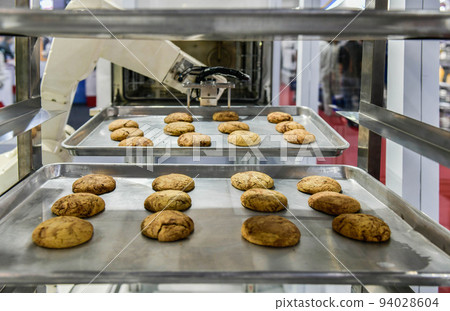 Robot arm preparing cookies for the oven in production line factory, industrial food production. Robot arm preparing cookies for the oven in production line factory, industrial food production. 94028604