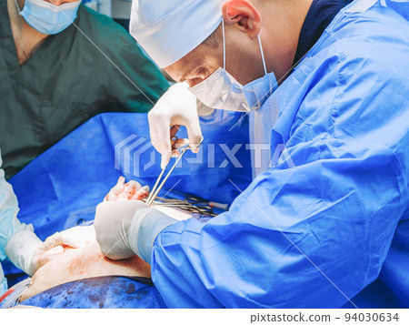 A male surgeon close-up operates on a patient with surgical instruments. A male surgeon close-up operates on a patient with surgical instruments. 94030634