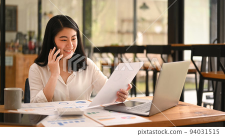 Professional female advisor reading document and consulting client on cellphone at her office desk 94031515