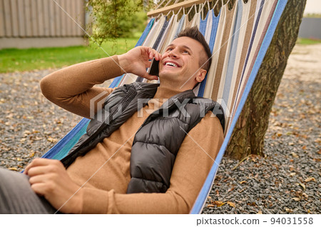 Joyous vacationer having a phone conversation outdoors Joyous vacationer having a phone conversation outdoors 94031558
