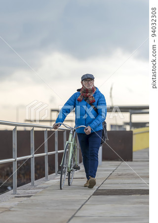 Handsome senior man walking with bike on seafront Handsome senior man walking with bike on seafront 94032308