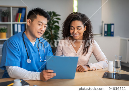 Happy senior chinese man with tablet consulting young african american female patient in clinic office interior 94036511
