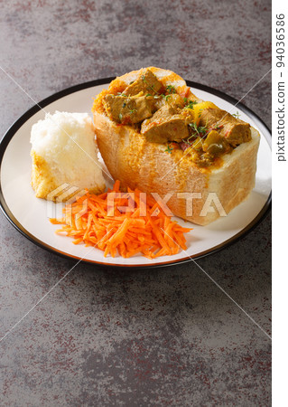 Durban Bunny Chow or a quarter mutton bunny consisting of a section of a loaf of bread hollowed out and filled with mutton curry and gravy closeup on plate. Vertical 94036586
