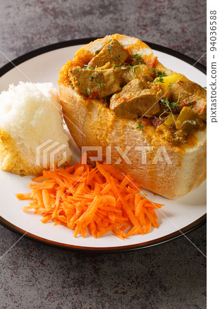 South African Bunny Chow bread stuffed with lamb curry with vegetables close-up on a plate. vertical 94036588
