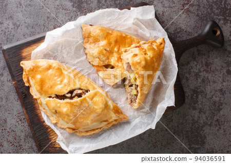 Cornish Pasty Baked pie filled with meat and potatoes closeup on the wooden board. Horizontal top view Cornish Pasty Baked pie filled with meat and potatoes closeup on the wooden board. Horizontal top view 94036591