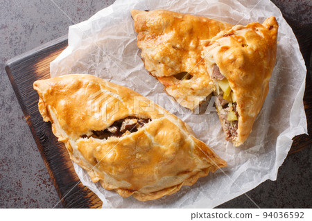 Traditional Cornish pasty filled with meat potato swede and carrot closeup on the paper. Horizontal top view Traditional Cornish pasty filled with meat potato swede and carrot closeup on the paper. Horizontal top view 94036592