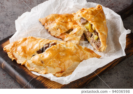Cornish Pasty Baked pie filled with meat and potatoes closeup on the wooden board. Horizontal 94036598