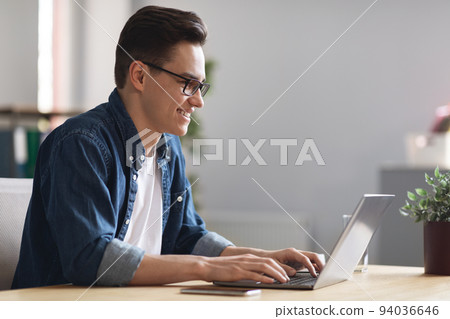 Young Male Company Employee Working With Laptop In Office, Side View 94036646