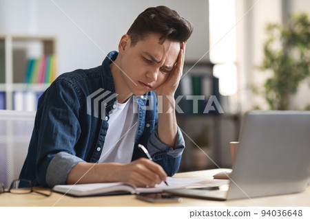 Young male entrepreneur massaging temple, suffering headache at workplace in office 94036648