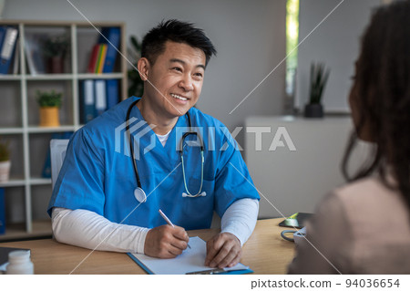 Cheerful friendly mature korean man doctor consulting young african american lady patient in clinic 94036654