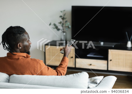 African american man watching television, pointing remote control at empty TV screen, mockup African american man watching television, pointing remote control at empty TV screen, mockup 94036834