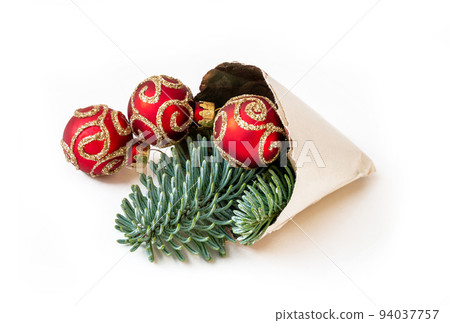 Paper cone with Christmas decorative fresh fir twigs and three shiny red balls on white background Paper cone with Christmas decorative fresh fir twigs and three shiny red balls on white background 94037757