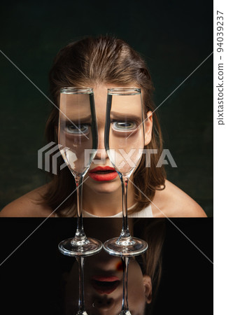 Contemporary art portrait of pretty girl looking through wine glasses over dark background. Weird emotions. Concept of art, creativity, surrealism. Closeup 94039237