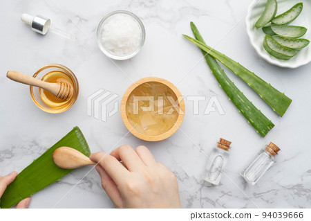 Natural homemade aloe vera gel face and body scrub for skin problems. DIY Recipe for sunburn, acne and dry skin. Top view of aloe vera, honey, sea salt and essential oil bottle on marble background. Natural homemade aloe vera gel face and body scrub for skin problems. DIY Recipe for sunburn, acne and dry skin. Top view of aloe vera, honey, sea salt and essential oil bottle on marble background. 94039666