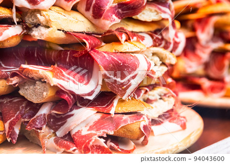 traditional Spanish bocadillos with Iberico jamon laid out in a slide on a shop window 94043600