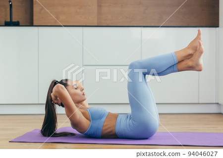 Sports time. Young beautiful fitness woman doing exercises at home on the mat, lifts her legs, shakes the press, squeezes 94046027