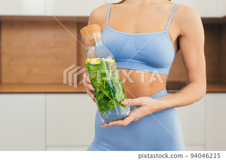 Close up photo part of body of young fitness woman holding and showing bottle of fresh juice, detox at home Close up photo part of body of young fitness woman holding and showing bottle of fresh juice, detox at home 94046215