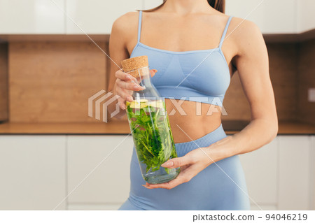 Close up photo part of body of young fitness woman holding and showing bottle of fresh juice, detox at home Close up photo part of body of young fitness woman holding and showing bottle of fresh juice, detox at home 94046219