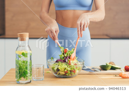 Close up photo, body part, hands of young fitness woman making salad with fresh vegetables and fresh detox drink in kitchen at home Close up photo, body part, hands of young fitness woman making salad with fresh vegetables and fresh detox drink in kitchen at home 94046313