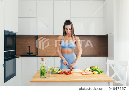Young sporty woman prepares healthy food in the kitchen at home, cuts vegetables Young sporty woman prepares healthy food in the kitchen at home, cuts vegetables 94047267