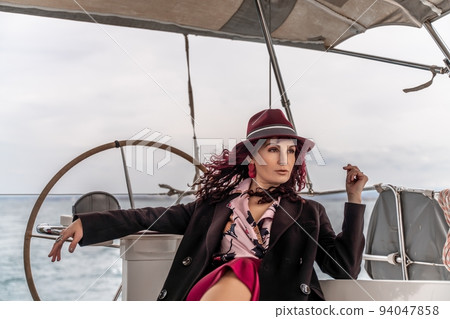 Attractive middle-aged woman at the helm of a yacht on a summer day. Luxury summer adventure, outdoor activities. 94047858