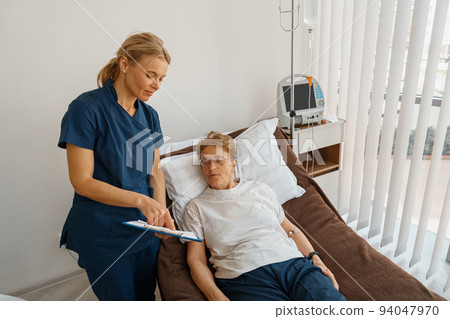 Nurse in uniform explain to patient results of analysis standing in hospital ward Nurse in uniform explain to patient results of analysis standing in hospital ward 94047970