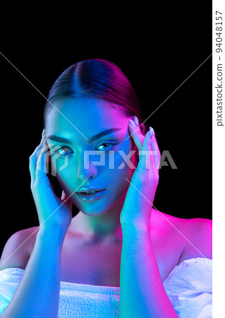 Closeup young beautiful woman with well-kept skin and sophisticated facial features isolated over dark background in purple neon light. 94048157