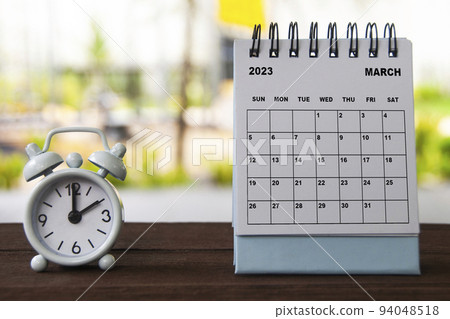 Alarm clock pointing at 2 o'clock with March calendar on a bench. Time and calendar concept Alarm clock pointing at 2 o'clock with March calendar on a bench. Time and calendar concept 94048518