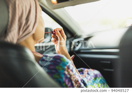 Woman looking in rear view mirror painting her lips doing applying make up in car. Woman looking in rear view mirror painting her lips doing applying make up in car. 94048527