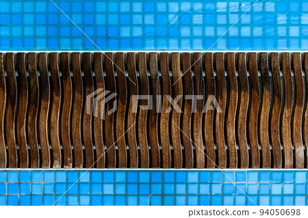 Close-up detail view of wet wooden pool edge overflow drain grain in blue mosaic tile. Abstract pattern of luxury poolside wood drainage grate. SPA water at hotel service and maintenance concept 94050698
