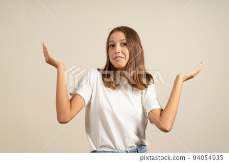 Close up portrait of brunette teenage girl with raised hands in indignation gesture isolated over beige background. Copy space. 94054935