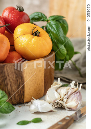 Wooden bowl of fresh colorful tomatoes, garlic, basil, pepper and olive oil on textured background. Kitchen still life in rustic style 94055070