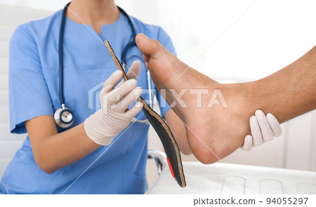 Female orthopedist fitting insole on patient's foot in clinic, closeup Female orthopedist fitting insole on patient's foot in clinic, closeup 94055297
