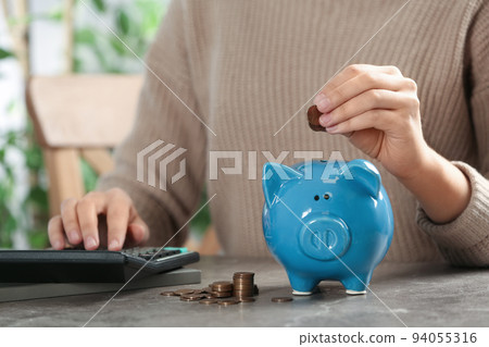 Woman putting money into piggy bank at table, closeup 94055316