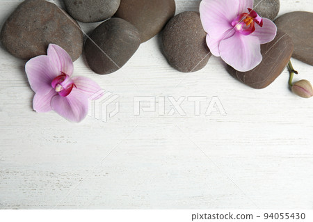 Stones with orchid flowers and space for text on white wooden background, flat lay. Zen lifestyle Stones with orchid flowers and space for text on white wooden background, flat lay. Zen lifestyle 94055430