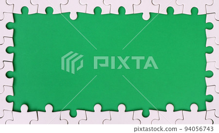 Framing in the form of a rectangle, made of a white jigsaw puzzle around the green space Framing in the form of a rectangle, made of a white jigsaw puzzle around the green space 94056743