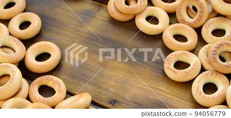 A lot of fresh yellow bagels lie on the surface of the old dark wood. A popular kind of flour products. One of the traditional Russian treats for tea A lot of fresh yellow bagels lie on the surface of the old dark wood. A popular kind of flour products. One of the traditional Russian treats for tea 94056779