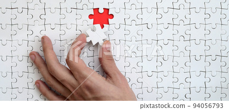 The texture of a white puzzle puzzle in the assembled state with one missing element that the male hand puts in The texture of a white puzzle puzzle in the assembled state with one missing element that the male hand puts in 94056793