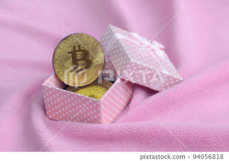 The golden bitcoin lies in a small pink gift box with a small bow on a blanket made of soft and fluffy light pink fleece fabric with a large number of relief folds The golden bitcoin lies in a small pink gift box with a small bow on a blanket made of soft and fluffy light pink fleece fabric with a large number of relief folds 94056818
