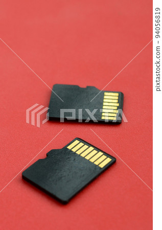 Two small micro SD memory cards lie on a red background. A small and compact data and information store 94056819