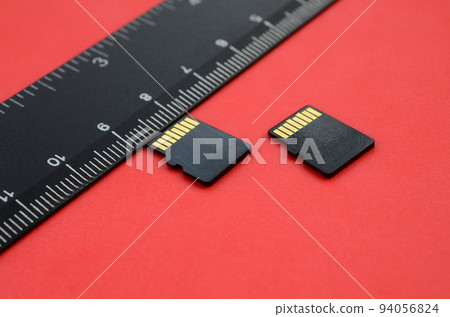 Two small micro SD memory cards lie on a red background next to a black ruler. A small and compact data and information store 94056824