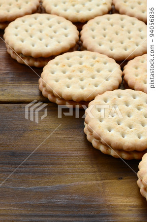 A round sandwich cookie with coconut filling lies in large quantities on a brown wooden surface. Photo of edible treats on a wooden background with copy space A round sandwich cookie with coconut filling lies in large quantities on a brown wooden surface. Photo of edible treats on a wooden background with copy space 94056836