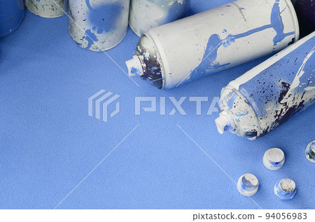 Some used blue aerosol spray cans and nozzles with paint drips lies on a blanket of soft and furry light blue fleece fabric. Classic female design color. Graffiti hooliganism concept Some used blue aerosol spray cans and nozzles with paint drips lies on a blanket of soft and furry light blue fleece fabric. Classic female design color. Graffiti hooliganism concept 94056983