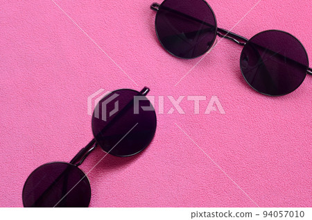 Two stylish black sunglasses with round glasses lies on a blanket made of soft and fluffy light pink fleece fabric. Fashionable background picture in female colors 94057010