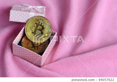 The golden bitcoin lies in a small pink gift box with a small bow on a blanket made of soft and fluffy light pink fleece fabric with a large number of relief folds The golden bitcoin lies in a small pink gift box with a small bow on a blanket made of soft and fluffy light pink fleece fabric with a large number of relief folds 94057022