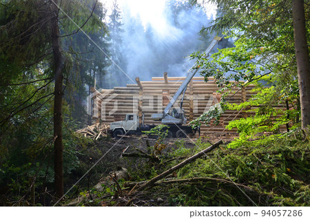 The process of building a wooden house from wooden beams of cylindrical shape. Crane in working condition 94057286